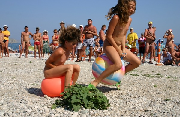 Family nudism - competition of young girls of nudists on jumps on a ball